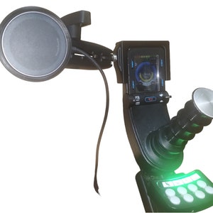 May include: A black and green joystick with a round base and a screen displaying a blue and green interface. The joystick is attached to a black mount with a microphone on the side.