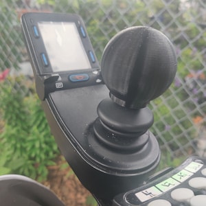 May include: A black joystick with a round, gray knob and a small screen with the word "OFF" displayed. The joystick is mounted on a black base with a series of buttons.