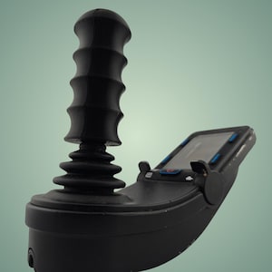 May include: A black joystick controller with a textured handle and a display screen. The controller has a base with buttons and a screen, and is designed for use with a mobility device.