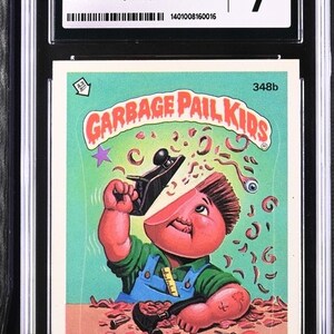 May include: A Garbage Pail Kids trading card featuring a cartoon character with a red face and brown hair, holding a wood plane and wearing a blue and green shirt. The card is green and white with the text "Garbage Pail Kids" and "Woody Shop" in large, bold letters.