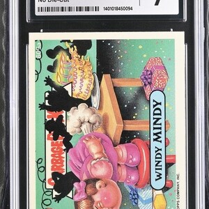 May include: A trading card featuring a cartoon character named Windy Mindy from the Garbage Pail Kids series. She is wearing a pink dress and has a large, red, puffy face. She is sitting on a red stool with a birthday cake and a present behind her. The card is from the 1988 Topps Garbage Pail Kids series, number 605a.
