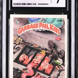 May include: A Garbage Pail Kids trading card featuring a pink baby with a long tongue in a cage. The card is numbered 366b and the character's name is Sis Pool. The card is graded Near Mint 7 by CGC.