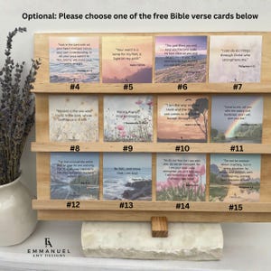 May include: A light-colored wooden display stand with three horizontal shelves holding twelve square cards, each featuring a unique landscape photograph and a printed Bible verse, numbered four through fifteen, with the text Emmanuel Amy Designs.
