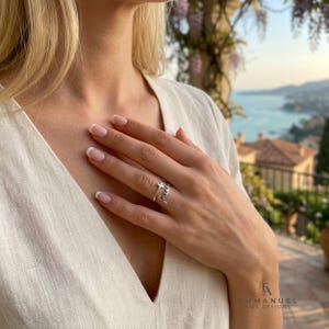 Peut inclure: Une bague argent&eacute;e orn&eacute;e d'une petite croix et du mot faith &eacute;crit en lettres cursives. La bague est port&eacute;e sur l'annulaire, mettant en valeur une finition m&eacute;tallique polie et un design &agrave; anneau ouvert qui entoure d&eacute;licatement le doigt.