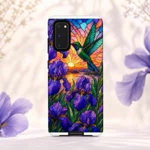 May include: A rectangular phone case featuring a stained glass style design of a green hummingbird in flight over a sunset landscape with purple iris flowers in the foreground. The case has a black camera cutout on the upper left side.