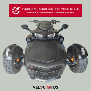 K&ouml;nnte beinhalten: Ein mattschwarzes Trike mit drei R&auml;dern, das ein schlankes Design und moderne Scheinwerfer aufweist. Das Bild enth&auml;lt den Text "YOUR BIKE, YOUR COLORS, YOUR STYLE" und "VELOCIMODS". Die Front des Trikes hat einen Wabenf&ouml;rmigen K&uuml;hlergrill.