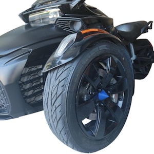 May include: A black three-wheeled motorcycle with a sleek design. The front wheel is large with a black rim and a blue center cap. The vehicle has a matte black finish and a headlight.