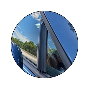 Peut inclure: Une garniture de montant automobile noire installée sur l'extérieur du cadre de porte d'un véhicule bleu. Le composant est positionné verticalement le long du bord de la fenêtre, avec une finition sombre et lisse contrastant avec la carrosserie.