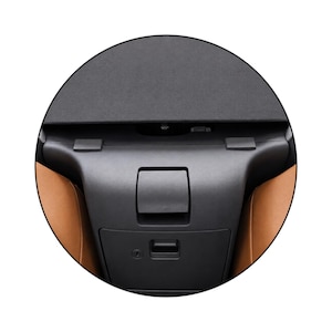 May include: A black plastic automotive center console component featuring a central latch mechanism, a lower storage compartment with a keyhole, and two top mounting tabs, flanked by tan-colored interior panels on the left and right sides.