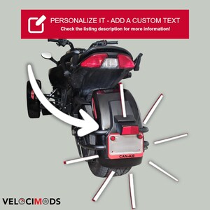 K&ouml;nnte beinhalten: Schwarzes und rotes Can-Am Dreiradmotorrad mit dem Text "PERSONALIZE IT - ADD A CUSTOM TEXT" in einem roten Banner. Das Bild enth&auml;lt auch den Text "Weitere Informationen finden Sie in der Angebotsbeschreibung!" und "VELOCIMODS".