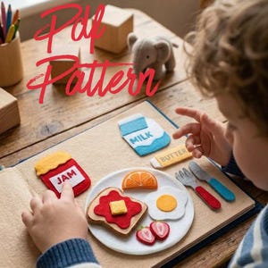 May include: A felt play food set featuring a white plate with toast topped with red jam and a yellow butter square, a fried egg, orange slice, and strawberry halves. Includes felt milk carton, butter stick, and cutlery with red and blue handles.