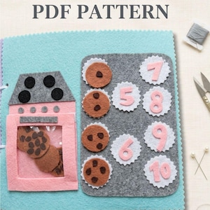 Może przedstawiać: Projekt rękodzielniczy z filcu z napisem PDF PATTERN na jasnoniebieskim tle, z różowym piekarnikiem zawierającym brązowe ciasteczka. Szara prostokątna mata prezentuje cztery ciasteczka oraz białe faliste koła z różowymi cyframi od pięciu do dziesięciu.