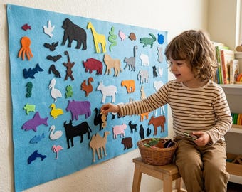 May include: A large light blue felt board mounted on a wall, featuring numerous colorful felt animal shapes including a gorilla, giraffe, camel, and various sea creatures. A woven basket sits on a wooden stool, containing additional felt animal pieces.
