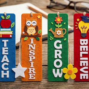 Puede incluir: Cuatro marcapáginas rectangulares de fieltro en azul, naranja, verde y rojo. El marcapáginas azul presenta una pila de libros y una manzana con la palabra TEACH. El naranja muestra un búho con INSPIRE. El verde muestra una regadera con GROW. El rojo tiene una bombilla y un birrete con BELIEVE.
