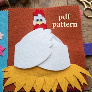 May include: A felt craft project featuring a white chicken with a red comb and wattle, sitting in a yellow felt nest on a brown background. The text "pdf pattern" is printed in white. The scene includes sewing spools and gold scissors.
