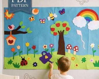May include: A large blue and green felt wall hanging featuring a landscape scene with a rainbow, clouds, a tree with red apples, a birdhouse, flowers, a ladybug, a bee, and a purple watering can. A blue banner at the top reads PDF PATTERN.