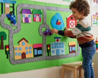 May include: A large green felt wall hanging featuring a road network, colorful houses, a hospital, a barn, a pond with a boat, traffic lights, and trees. The set includes detachable felt vehicles and buildings that can be arranged on the surface.