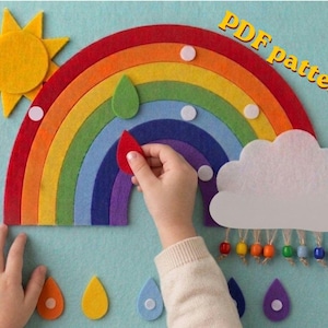 May include: A felt rainbow craft project featuring a yellow sun, a multi-coloured arched rainbow with white circular accents, and a white cloud with dangling colourful beads. The text PDF pattern is visible in the upper right corner.