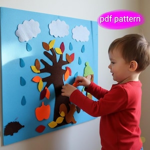 Puede incluir: Un tablero de fieltro azul con un árbol marrón, hojas coloridas, nubes blancas y gotas de lluvia azules. Un niño con una camisa roja interactúa con el tablero, agregando hojas naranjas. El texto "pdf pattern" es visible.