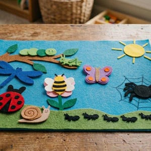 May include: A rectangular blue felt board featuring various colorful felt insect and nature shapes including a ladybug, snail, bee on a flower, dragonfly, butterfly, spider on a web, a green caterpillar on a brown branch, and a line of black ants.