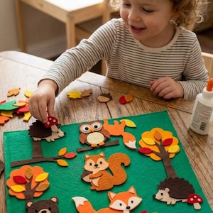 Op de afbeelding: Een groen viltbord met diverse bosdieren en natuurvormen, waaronder een bruine beer, een eekhoorn met een eikel, een vos, een uil en twee egels met rode paddenstoelen, samen met kleurrijke herfstbladeren en bomen.
