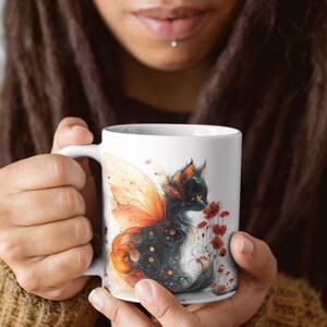 Op de afbeelding: Witte keramische mok met een zwarte kat met vlinder vleugels en rode bloemen erop gedrukt.