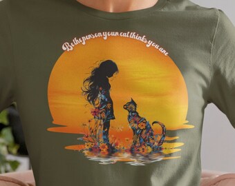 May include: A green t-shirt with a sunset graphic and the text "Be the person your cat thinks you are". The graphic features a silhouette of a girl and a cat standing in the water.