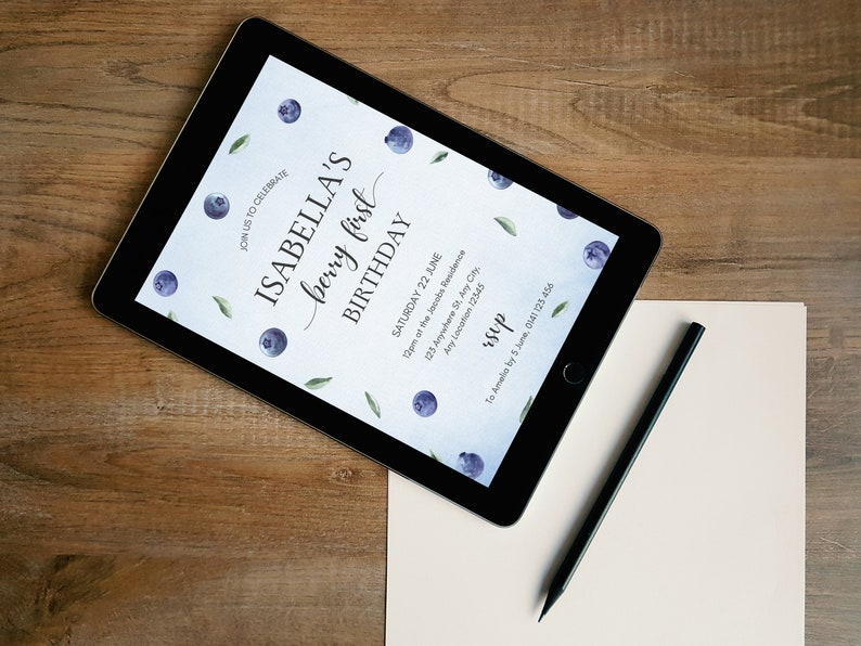 May include: A digital invitation on a tablet screen for Isabella's first birthday party. The invitation features a watercolor design with blueberries and leaves on a light blue background. The text reads "Join us to celebrate Isabella's berry first birthday. Saturday 22 June. 12pm of the Jacobs Residence. 123 Anywhere St. Any City. Any Location 12545. RSVP to Amelis by 5 June, 0141125 456."