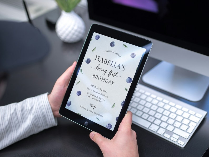 May include: A digital tablet displaying a blue and green birthday invitation with the text "JOIN US TO CELEBRATE ISABELLA'S berry first BIRTHDAY SATURDAY 22 JUNE 123 Anywhere St Any City Any Location 12343 RSVP 14 Amelia Dr, 5 June, 0123 456"