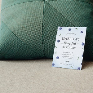 May include: A blue and white birthday invitation with a watercolor blueberry design. The invitation reads "Join us to celebrate Isabella's berry first birthday. Saturday 22 June 12pm at the Isabelle Residence 123 Anywhere St, Any City, Any Location 12345 RSVP To Amelia by 5 June, 0123 123 456".