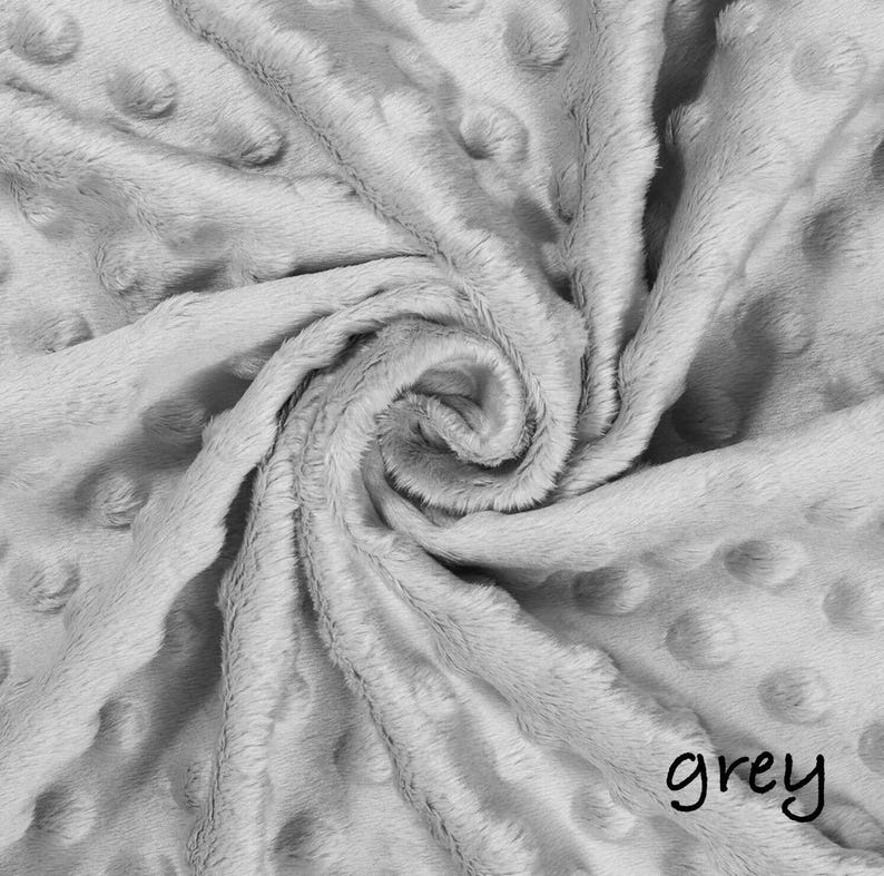May include: A close-up of a soft, gray blanket with a textured surface and a swirl pattern. The blanket has a dotted pattern and the word "grey" is written in the bottom right corner.