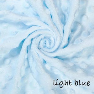 May include: A light blue, plush blanket with a swirl pattern. The blanket has a soft, textured surface with small, raised dots. The words "light blue" are written in black script in the lower right corner.