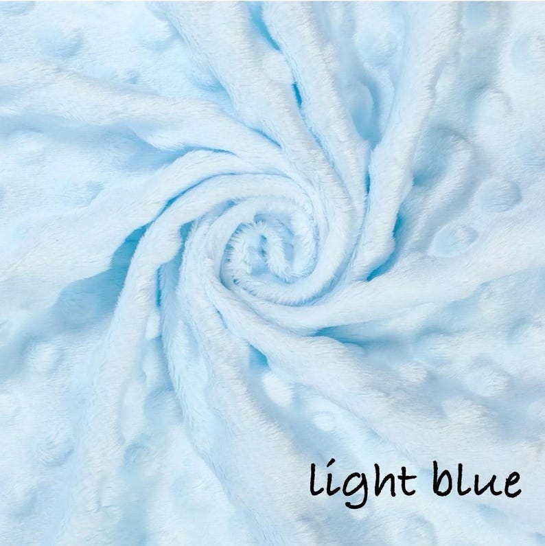 May include: A light blue, plush blanket with a swirl pattern. The blanket has a soft, textured surface with small, raised dots. The words "light blue" are written in black script in the lower right corner.