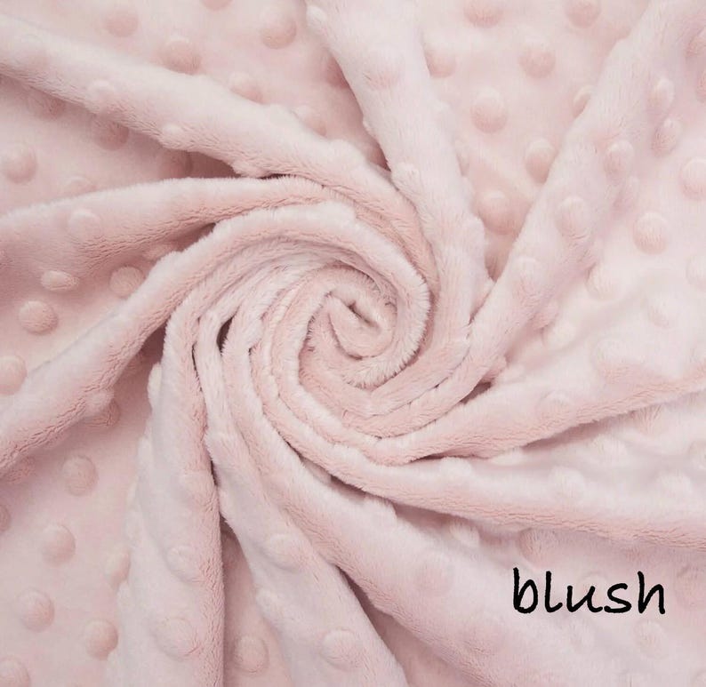 May include: A close-up of a soft, blush-colored fabric with a textured, dotted pattern. The fabric is swirled, creating a spiral effect. The word "blush" is written in a black script font in the bottom right corner.