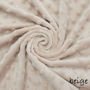 May include: Beige plush fabric with a textured, dotted pattern. The fabric is arranged in a spiral, with the word "beige" in a handwritten font in the bottom right corner. The material appears soft and inviting.