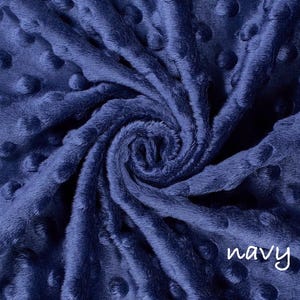 May include: Navy blue minky fabric with a swirl pattern. The fabric has a soft, plush texture with raised dot details. The word "navy" is written in a white script font in the lower right corner. This fabric is suitable for blankets and other craft projects.