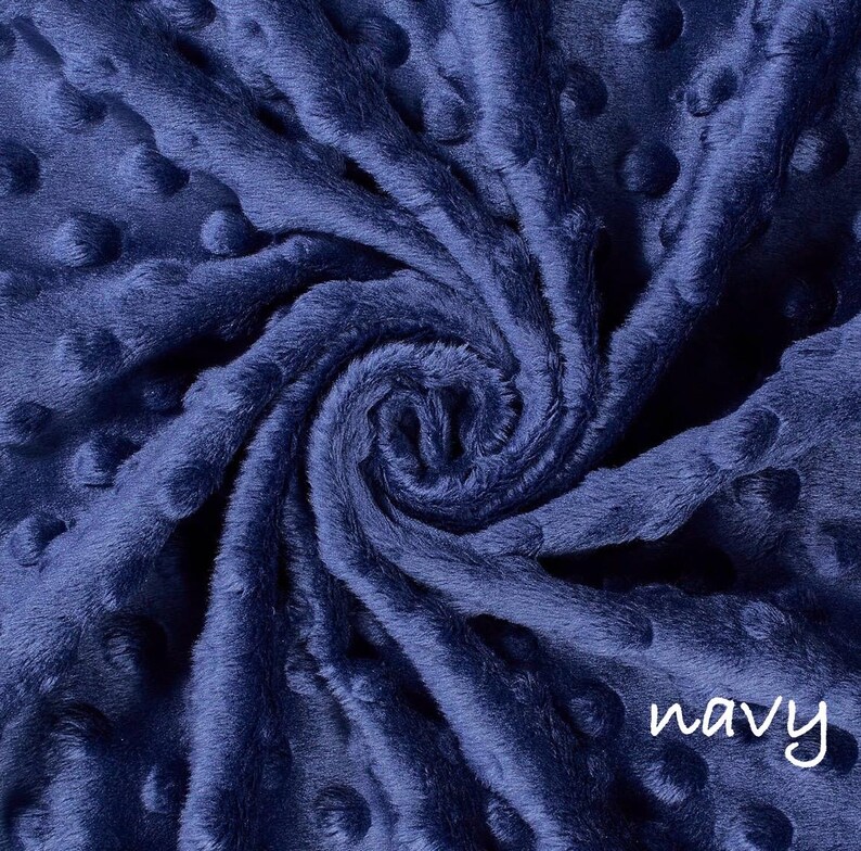 May include: Navy blue minky fabric with a swirl pattern. The fabric has a soft, plush texture with raised dot details. The word "navy" is written in a white script font in the lower right corner. This fabric is suitable for blankets and other craft projects.