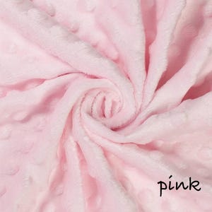 May include: A close-up of a soft, pink blanket with a textured, dotted pattern. The fabric is swirled, creating a spiral effect. The word "pink" is written in a handwritten font in the bottom right corner.