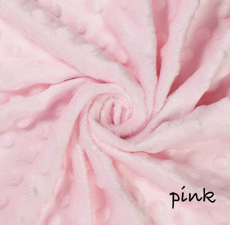 May include: A close-up of a soft, pink blanket with a textured, dotted pattern. The fabric is swirled, creating a spiral effect. The word "pink" is written in a handwritten font in the bottom right corner.