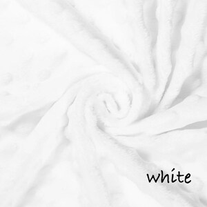 May include: A close-up shot of a soft, white blanket with a swirling pattern. The blanket has a plush texture and is made of a fluffy material. The word "white" is written in a black, cursive font in the bottom right corner.