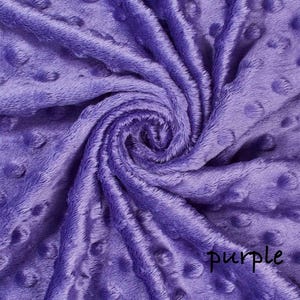 May include: A close-up of a soft, textured fabric in a vibrant purple hue. The fabric has a plush, velvety appearance with a pattern of raised, circular dots. The word "purple" is written in a cursive script on the fabric.