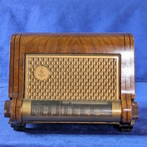 May include: Vintage wooden radio with a gold-colored speaker grill and a tuning dial. The radio has a dark wood finish with a rectangular shape and a curved top. The dial displays frequency numbers. The radio has the Zenith logo.