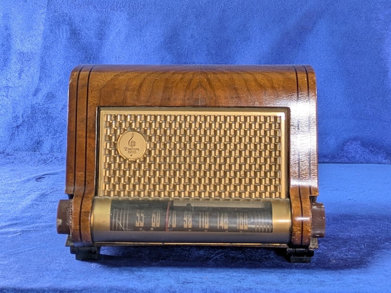 May include: Vintage wooden radio with a gold-colored speaker grill and a tuning dial. The radio has a dark wood finish with a rectangular shape and a curved top. The dial displays frequency numbers. The radio has the Zenith logo.