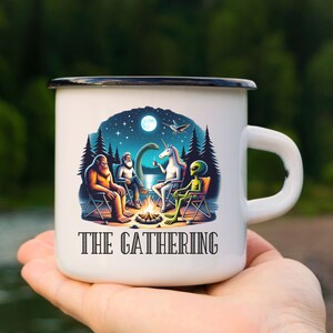 May include: White enamel camping mug with a black rim and handle. The mug features a colorful illustration of a Bigfoot, a unicorn, and an alien sitting around a campfire under a starry night sky. The text "THE GATHERING" is printed on the mug.