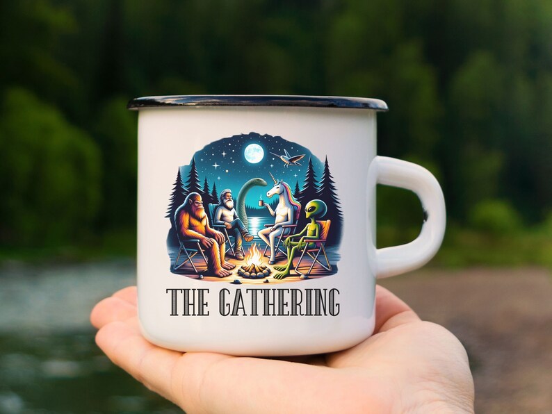 May include: White enamel camping mug with a black rim and handle. The mug features a colorful illustration of a Bigfoot, a unicorn, and an alien sitting around a campfire under a starry night sky. The text "THE GATHERING" is printed on the mug.