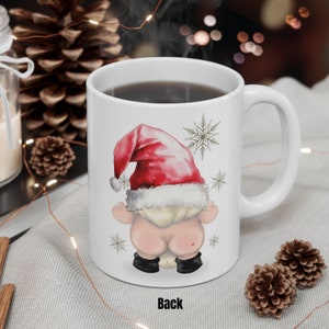 May include: White ceramic coffee mug featuring a red and white Santa hat gnome design. The gnome is facing away from the viewer with its back to the camera. The mug has the word "Back" printed on the bottom.