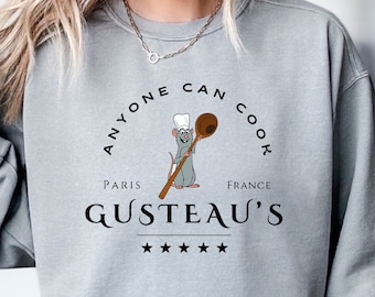 May include: A pale grey sweatshirt with the words "ANYONE CAN COOK" in a circular design, with "PARIS FRANCE" and "GUSTEAU'S" below. A cartoon rat chef holding a wooden spoon is in the center. Five stars are below the restaurant's name.