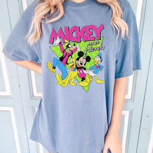May include: A blue t-shirt with the text "MICKEY and friends" in pink and white, featuring cartoon characters Mickey Mouse, Goofy, Pluto, and Donald Duck. The shirt has short sleeves and a loose fit.