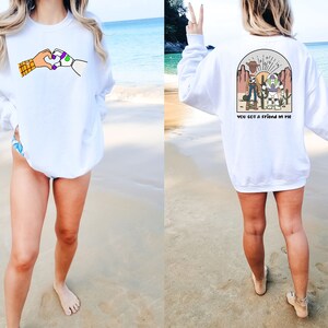 May include: White sweatshirt with a graphic of Woody and Buzz Lightyear from Toy Story on the front. The back of the sweatshirt has a graphic of Woody and Buzz Lightyear with the text "You got a friend in me".