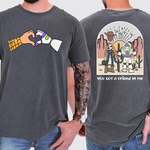 May include: A dark grey t-shirt with a cartoon image of Woody and Buzz Lightyear from Toy Story on the back. The back of the shirt also has the text "You got a friend in me". The front of the shirt has a cartoon image of Woody and Buzz Lightyear making a heart shape with their hands.